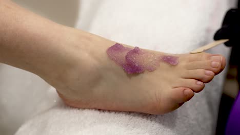 close-up pedicure: purple scrub applied to foot with spatula