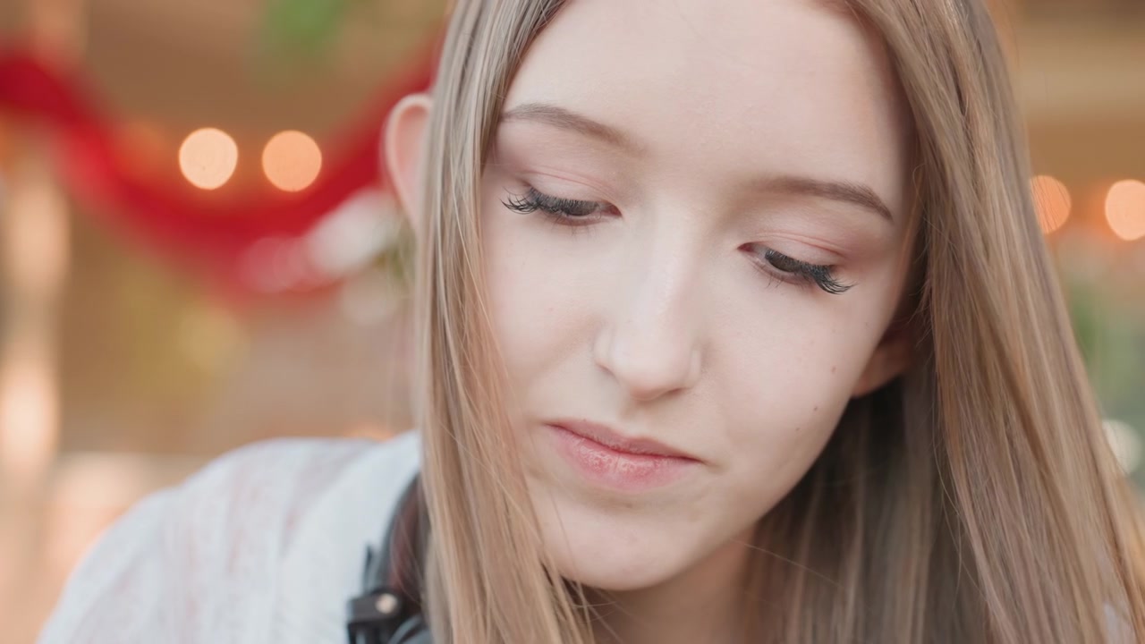 Close up of young woman with long blonde hair wearing light colored clothing and headphones. scene features soft lighting effects from blurred background lights creating bokeh circles
