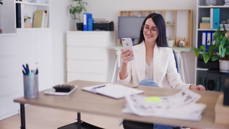 Happy-Businesswoman-Browsing-Internet-on-Smartphone-in-Office