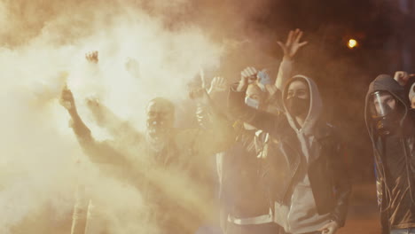 african american man with scarf on his face yelling with arms up and throwing molotov cocktail in a protest with multiethnic group of people in the street