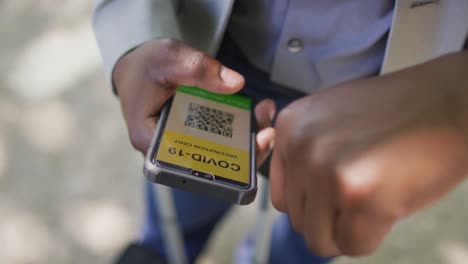 Hands-of-african-american-man-using-smartphone-with-covid-passport-and-smartwatch-in-city