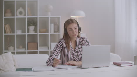 young woman is working remotely from home conducting negotiations online by video chat at laptop using headphones with mic