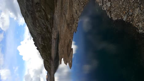 aerial flying over drone operator sitting on rock overlooking lake naret with blue sky and clouds reflected on surface