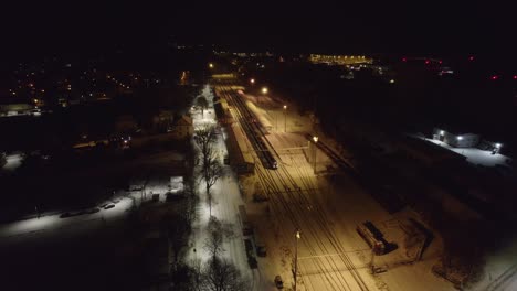 Departing-train-with-wagons-from-a-city-platform-in-winter-on-a-cold-night---static-drone-shot