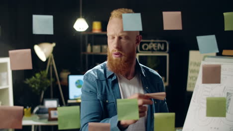 happy businessman sticking colorful papers on glass board in hipster office.