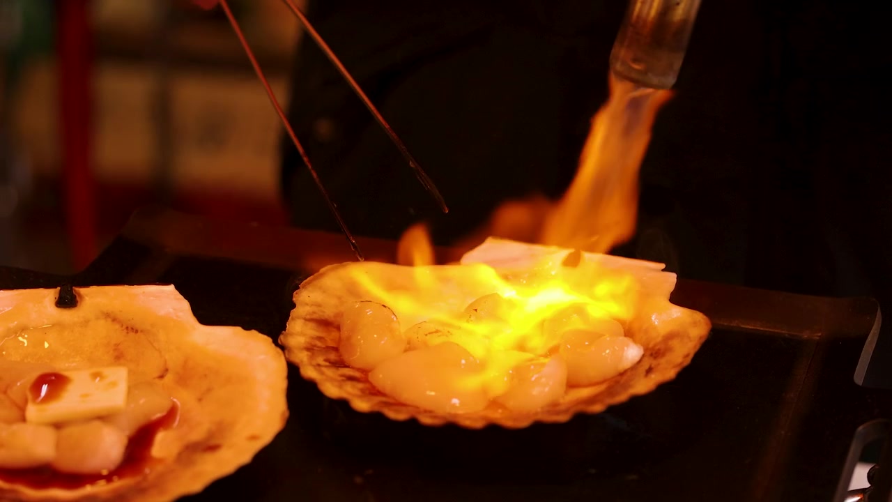 Close-up of scallops being seared with a blowtorch and butter at a Tokyo market.