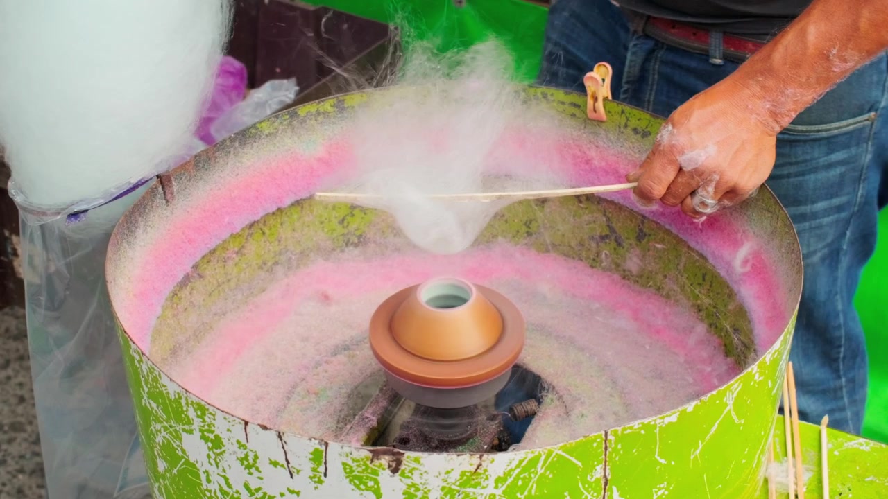 Sukkerspinnmaskin som spinner sukker ved en livlig tivolibod, middels oversiktsbilde.