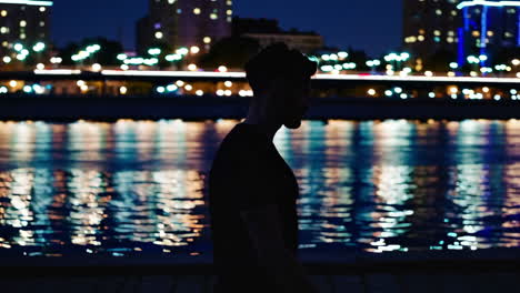 man walking along a river at night in a city