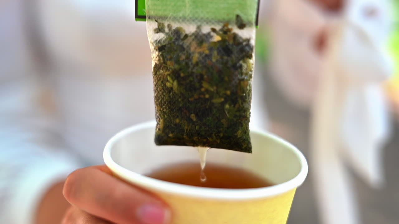 Woman stiring green tea bag into carton cup