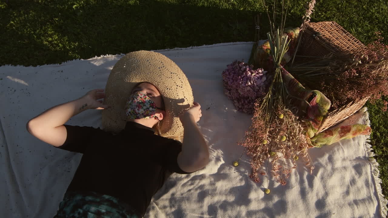 Fashionable girl applying face mask for coronavirus pandemic and lying down at the park