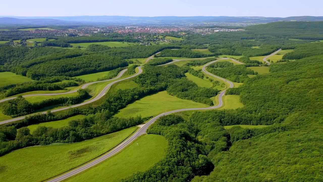 Een luchtfoto van weelderige groene glooiende heuvels en kronkelende wegen in een sereen landelijk landschap, die de schoonheid van de natuur toont met een schone achtergrond en voldoende kopieerruimte voor redactioneel gebruik