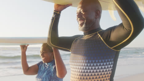 happy senior african american couple walking and holding surfboards at beach, in slow motion