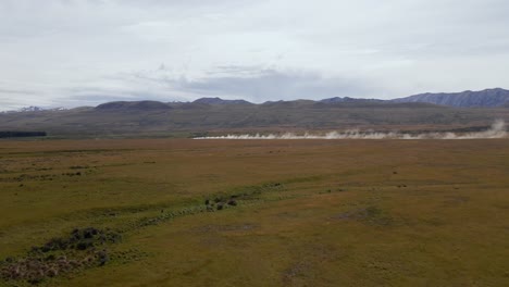 Mountains-and-meadows-on-sunny-day-with-vehicle-swirling-up-dust-on-distant-dirt-road