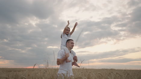 happy child and father are playing in field of ripening wheat. little daughter on fathers shoulders. baby boy and dad travel on field. kid and parent play in nature. happy family and childhood concept