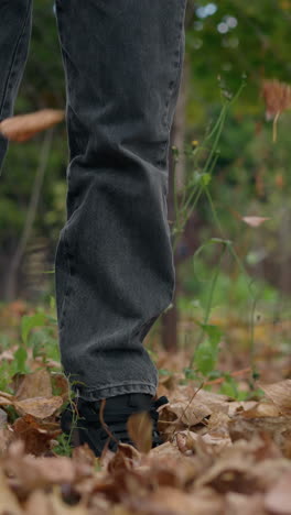 primer plano de una persona con pantalones de jean de pie en el bosque, vertiendo hojas secas en el suelo, con un fondo borroso de árboles en otoño, hojas de otoño esparcidas en el suelo