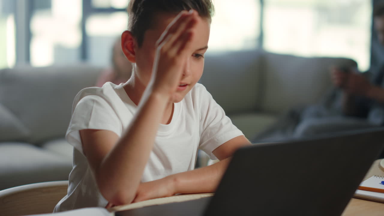 Kid raising hand during online class on laptop. Cheerful boy learning distance.