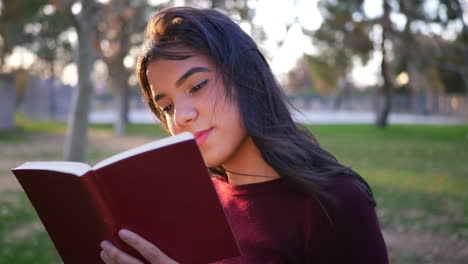 acercarse a una joven estudiante universitaria hispana leyendo las páginas de un libro de cuentos rojos o una novela al aire libre al atardecer a cámara lenta