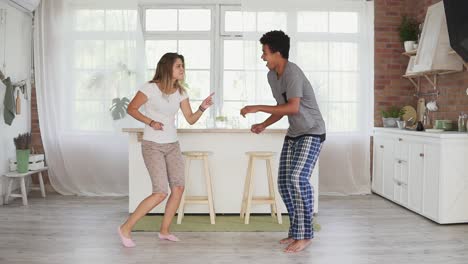 feliz pareja multiétnica bailando en la cocina en pijama. atractiva pareja enamorada divirtiéndose en casa. toma en cámara lenta