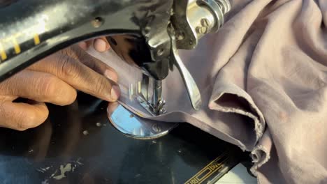 close up of indian tailor's hand stitching a cloth using vintage sewing machine