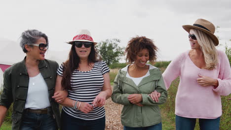 group of mature female friends walking along path through yurt campsite