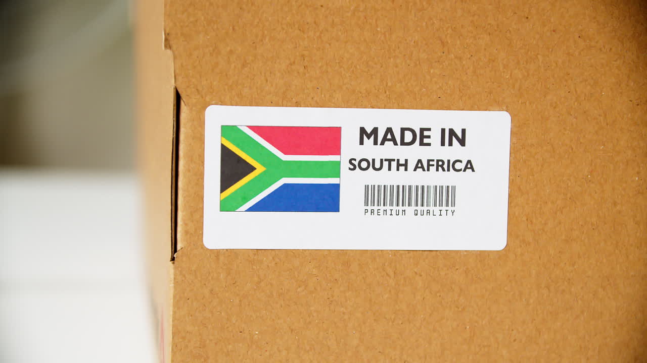 Hands applying MADE IN SOUTH AFRICA flag label on a shipping cardboard box with products