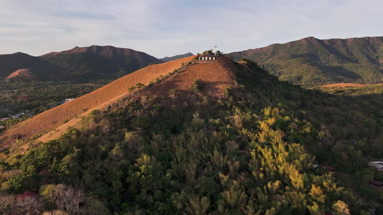 High above Coron Town in the Philippines, Mount Tapyas features a towering cross, bold CORON sign, winding trail, and sweeping mountain views surrounded by golden hills and lush forests