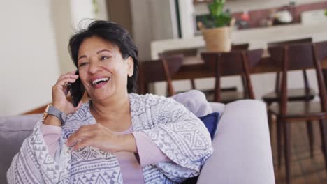 Mujer-Mayor-Afroamericana-Sonriendo-Mientras-Habla-Por-Teléfono-Inteligente-Sentada-En-El-Sofá-De-Casa