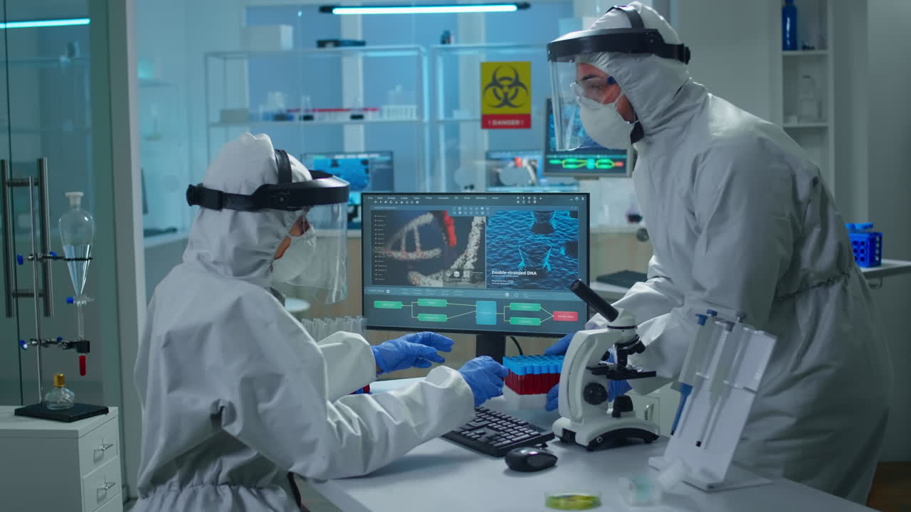 パソコンで働いているppeスーツの化学者実験室の技術者が彼女の血液サンプルをもたらしている間