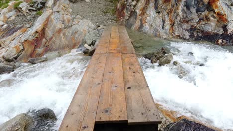 punto de vista de la pasarela de madera sin cuerdas que conduce al río alpino de flujo rápido