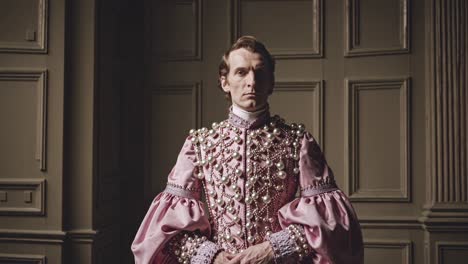 la recreación histórica presenta a un noble vestido con un elegante disfraz rosa, de pie en una habitación señorial con paneles de madera e iluminación sutil, evocando una sensación de gracia atemporal