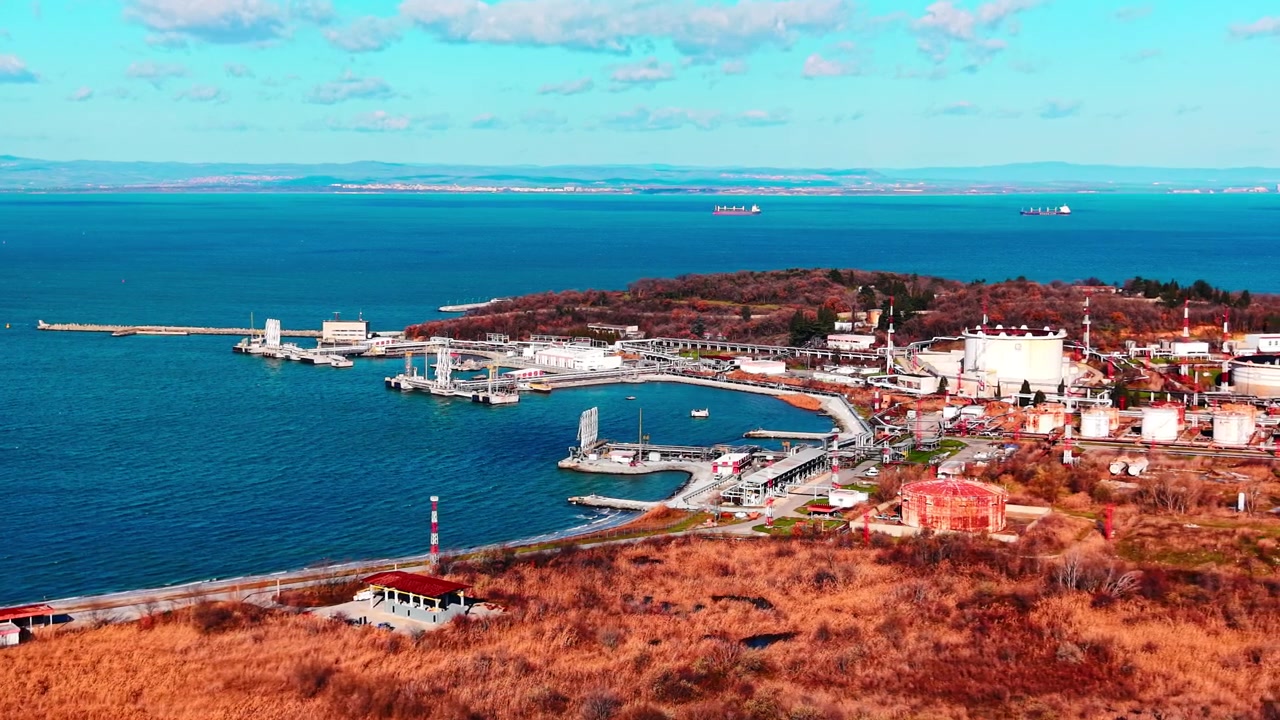Industrihavn med rørledninger og fragtskibe, Bulgarien. Luftfoto fra drone af en buet bølgebryder, læssekajer og turkist bugtvand