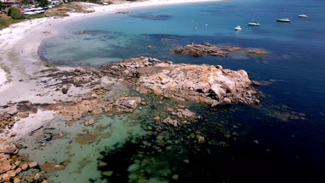 orbital shot of rocky shore with dark water and sailboats in sanxenxo spain