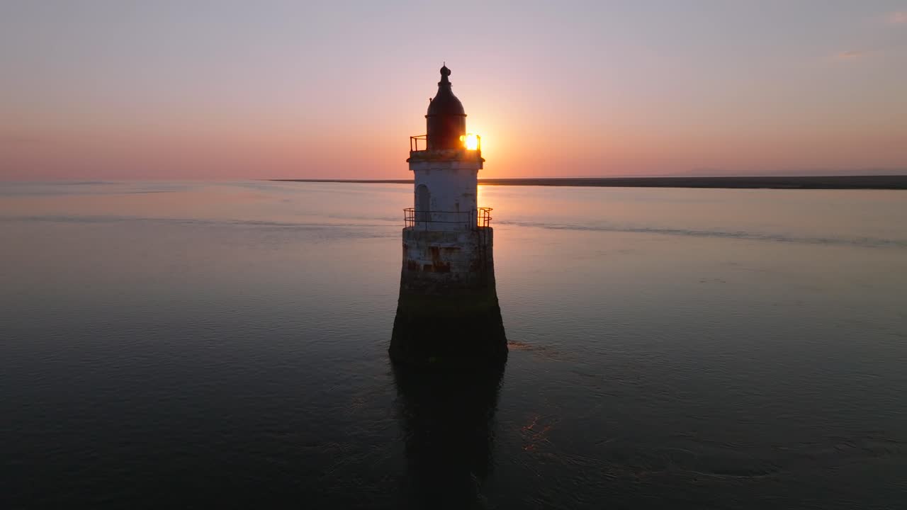Derelict lighthouse in very calm waters with setting sun being occluded. Plover Scar Lighthouse, Lancashire, UK.
