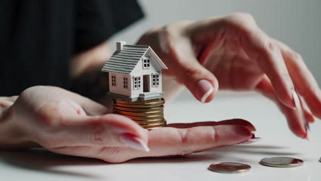 hands holding miniature house on coins