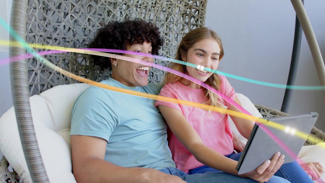 Pareja compartiendo una tableta en una silla huevo, pasando de sonreír a reír mientras cintas pasan por sus caras, tecnología.