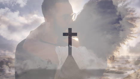 animation of cross on mountain against cloudy sky over diverse couple kissing on beach