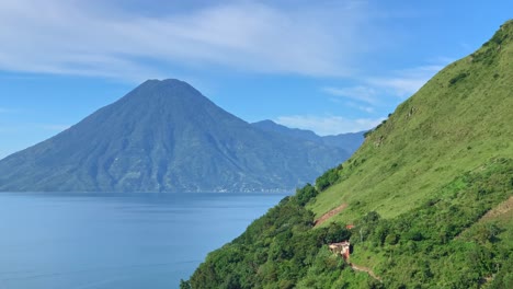 central american volcano volcan san pedro in lake atitlan, guatemala on a blue sunny day with boat traffic riding over the blue lake water and santa cruz la laguna green hillside in the foreground