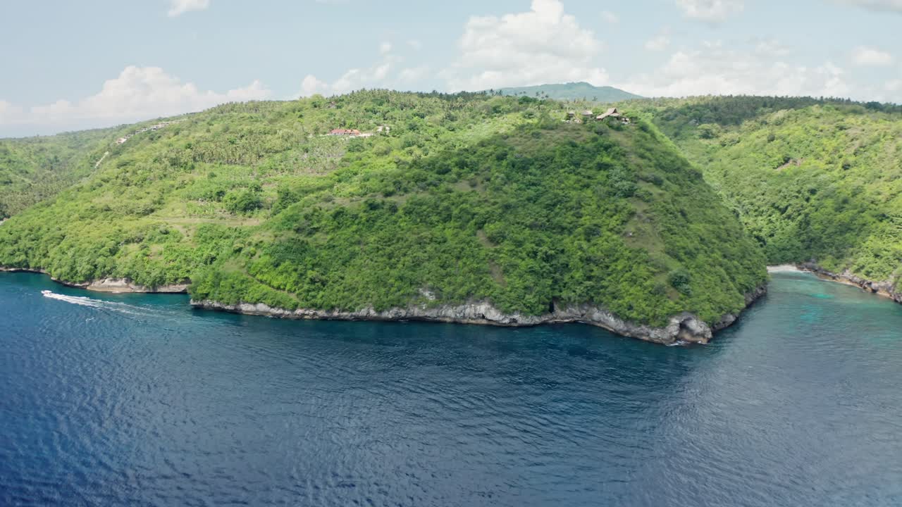 A sweeping aerial shot of the undeveloped, lush hilly coastline of Nusa Penida, Bali, Indonesia, showcasing the dense tropical greenery covering the undulating landscape