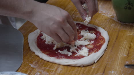 chef tops neapolitan pizza with mozzarella cheese, on wooden table