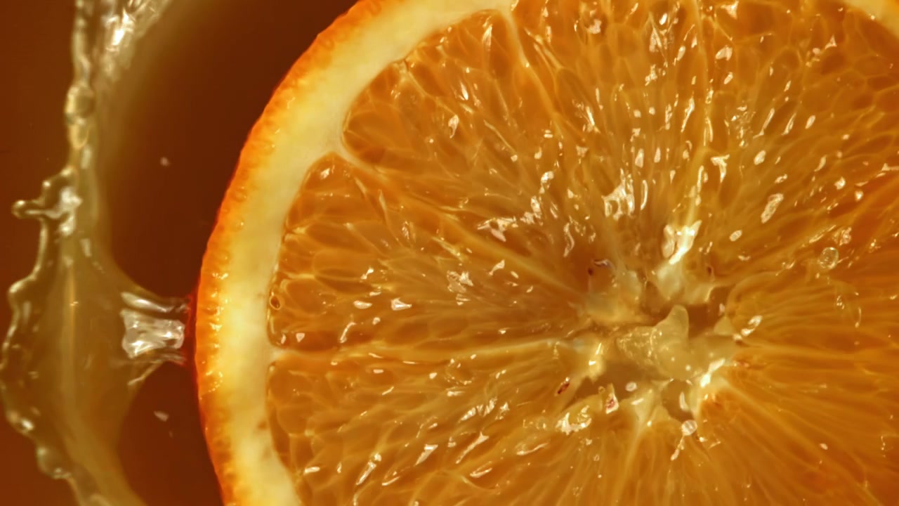 Primo piano di una fetta d'arancia che si tuffa nel succo al rallentatore