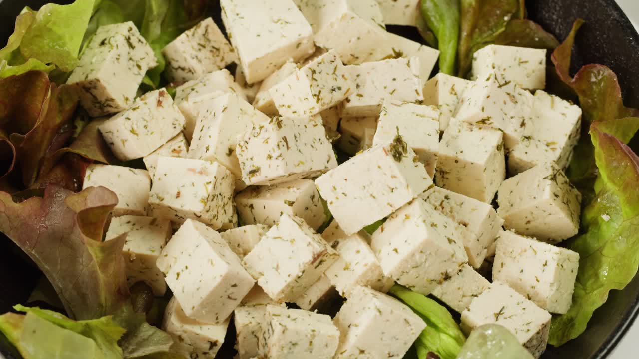 Fried tofu with sesame seeds and spices on cast iron pan, cooking japanese salad. Healthy ingredient for cooking vegan vegetarian diet food. Roasted tofu over black background.