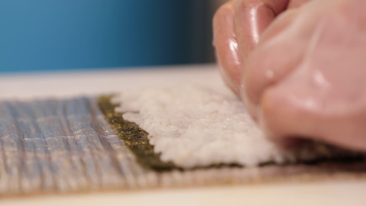 Chef Flattening The Japanese Rice On The Nori Seaweed For Sushi Rolls. - close up shot