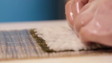 chef flattening the japanese rice on the nori seaweed for sushi rolls. - close up shot