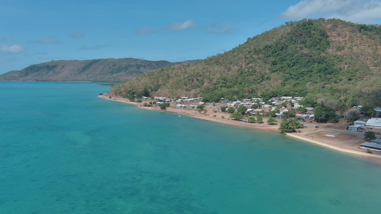 Aerial View, Palm island beach houses on the shoreline overlooking the blue ocean water with islands in the background on a sunny day.