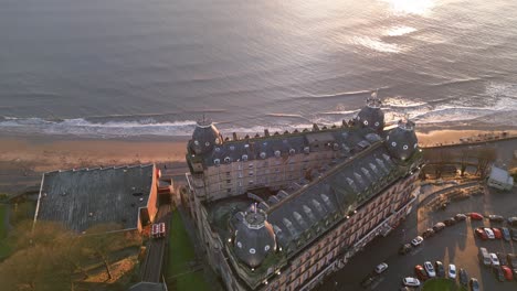 tomada superior del avión no tripulado del grand hotel situado al lado de una playa vacía con olas continuas en ella por la noche con algunos coches estacionados en scarborough north yorkshire, inglaterra