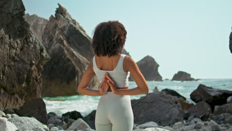 girl making namaste hands behind back on rocky seashore. woman stretching arms.