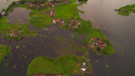 drone flying forwards revealing several humble houses on lawns surrounded by water after flooding