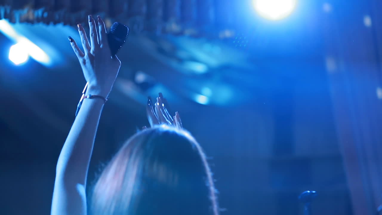 Beautiful girl with microphone singing on a concert with disco spotlights on the background