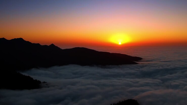 Sagome scure di montagne nella fitta coltre di nuvole bianche. Bellissimo sole al tramonto nel cielo arancione sullo sfondo. Vista aerea