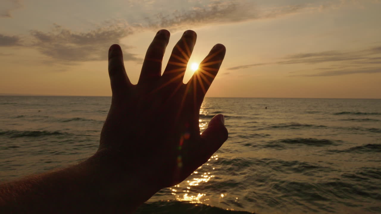 Sunlight Peeking Through Fingers of Hand at Sunset Over Ocean